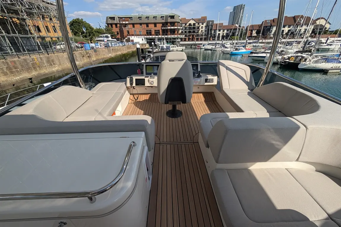 Interior of a luxury boat featuring seating, a helm, and marina views with moored yachts in the background.